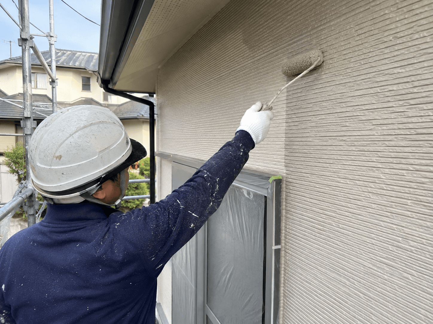 住宅外壁をローラーで塗装する職人